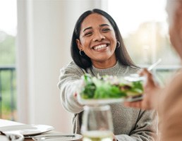 Woman smiling while grabbing dish from friend at table