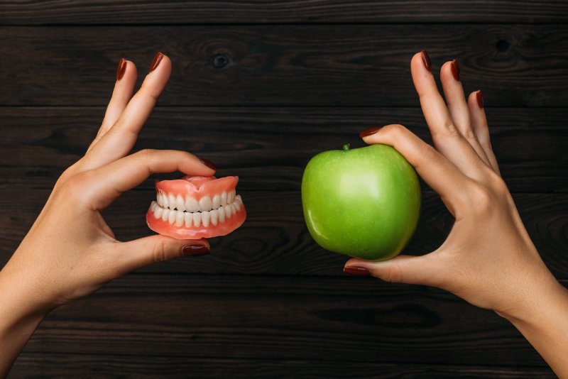 Two hands holding dentures and a green apple